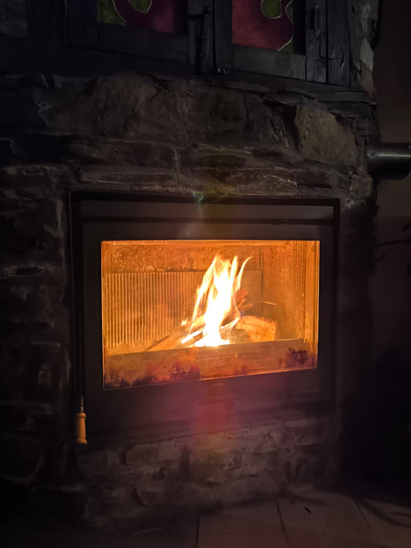Chimenea, ahora con la puerta cerrada, realza su función como fuente de calor eficiente y segura, manteniendo la magia de la llama visible. Este plano destaca la belleza de los materiales (piedra y metal) y la tranquilidad que aporta el fuego. Una imagen que transmite seguridad, confort y bienestar, garantizando un ambiente cálido y acogedor en cualquier momento.